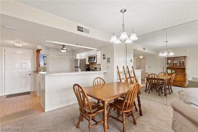 dining space featuring a textured ceiling, ceiling fan with notable chandelier, and light colored carpet