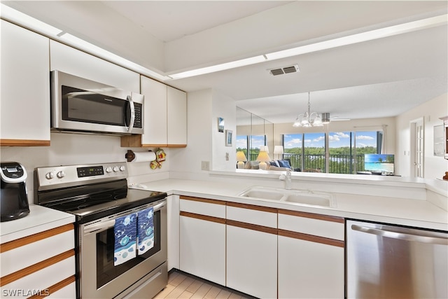 kitchen with stainless steel appliances, a notable chandelier, hanging light fixtures, sink, and white cabinets