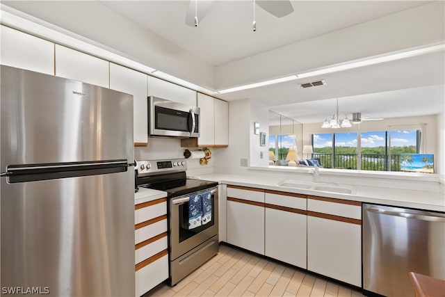 kitchen with stainless steel appliances, sink, white cabinetry, and ceiling fan with notable chandelier