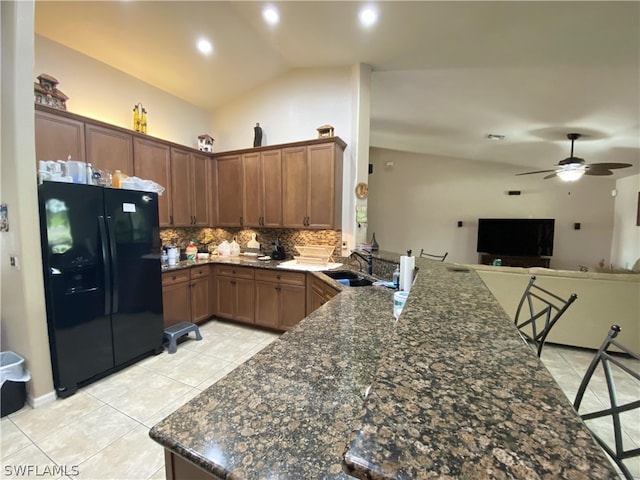 kitchen featuring kitchen peninsula, black refrigerator with ice dispenser, dark stone counters, vaulted ceiling, and sink