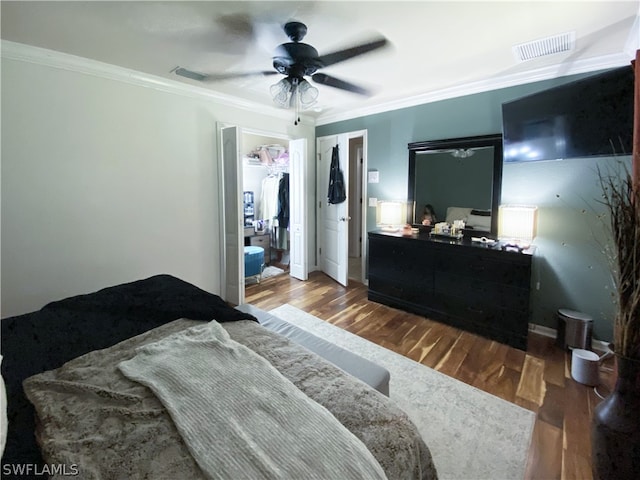 bedroom featuring ceiling fan, wood-type flooring, a walk in closet, a closet, and ornamental molding