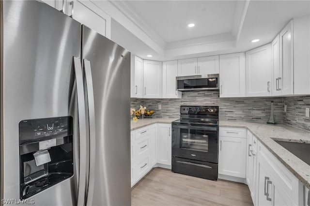 kitchen with stainless steel appliances, a raised ceiling, white cabinets, and light wood-style flooring