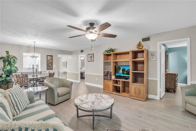 living room featuring ceiling fan with notable chandelier and light hardwood / wood-style flooring