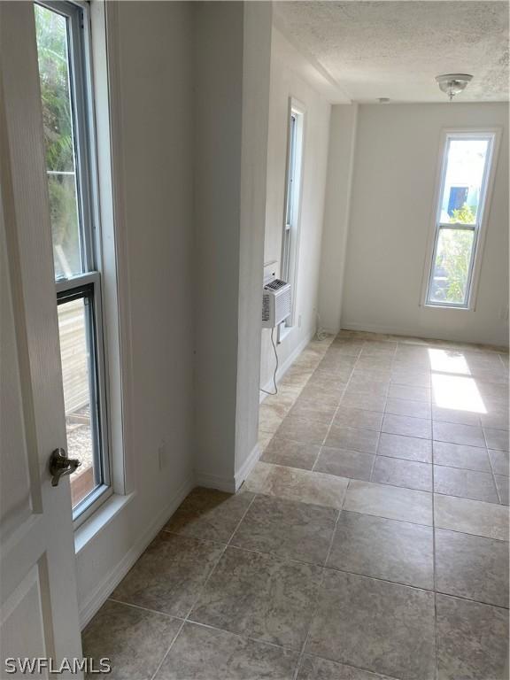 empty room with tile patterned floors, cooling unit, a textured ceiling, and baseboards