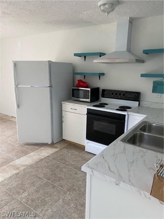 kitchen with electric stove, open shelves, stainless steel microwave, freestanding refrigerator, and wall chimney exhaust hood