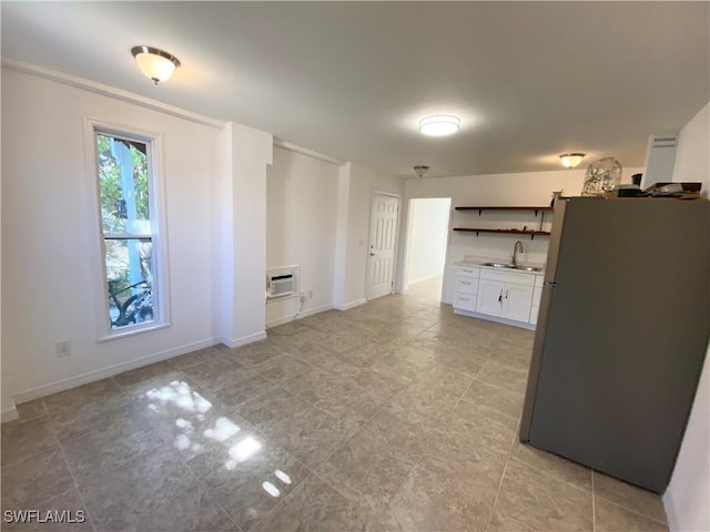 interior space featuring a wall mounted air conditioner, a sink, open shelves, white cabinetry, and freestanding refrigerator