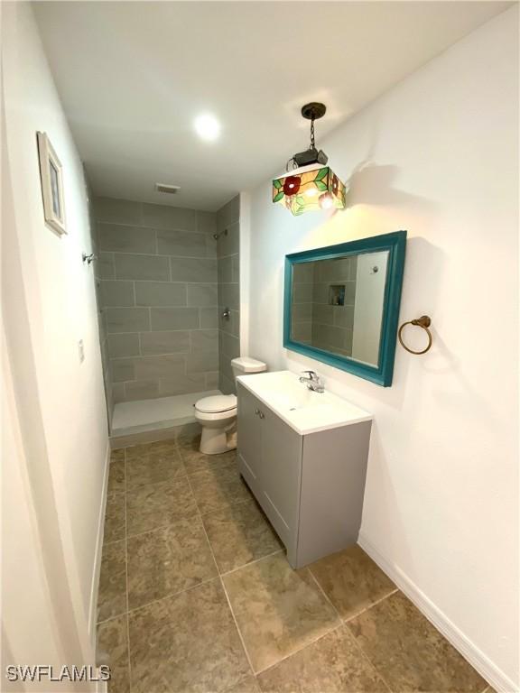 bathroom with vanity, toilet, and tiled shower