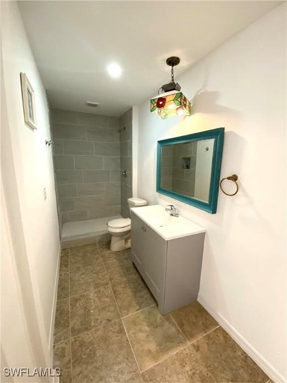 bathroom featuring a tile shower, toilet, vanity, and baseboards