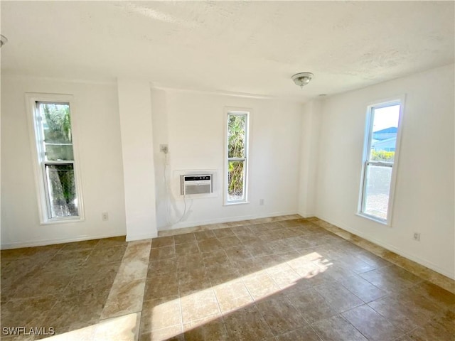 spare room with a wealth of natural light, a textured ceiling, a wall mounted air conditioner, and baseboards