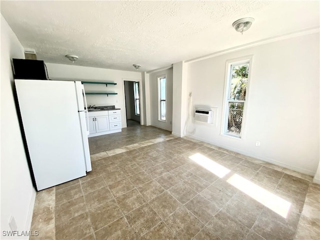 unfurnished living room with a wall mounted AC, baseboards, and a textured ceiling