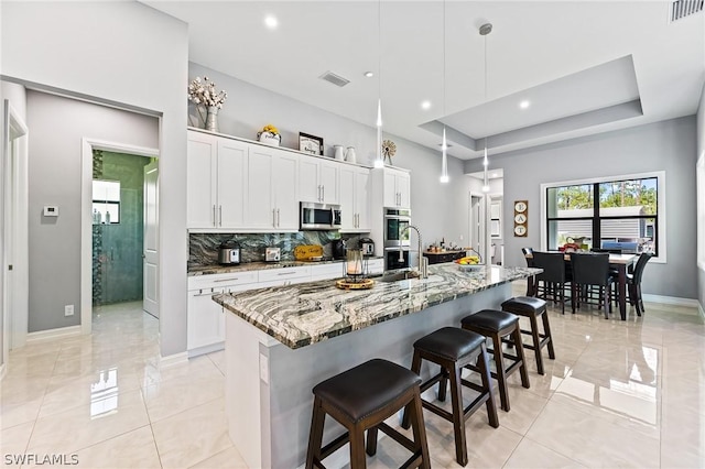 kitchen featuring a center island with sink, light stone countertops, decorative light fixtures, white cabinetry, and stainless steel appliances