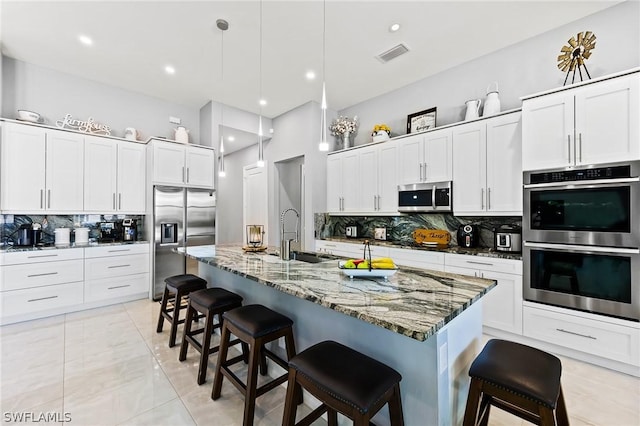 kitchen featuring a kitchen bar, backsplash, stainless steel appliances, a kitchen island with sink, and pendant lighting