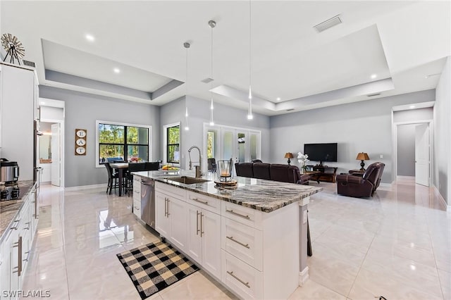 kitchen with a raised ceiling, white cabinetry, sink, and a kitchen island with sink