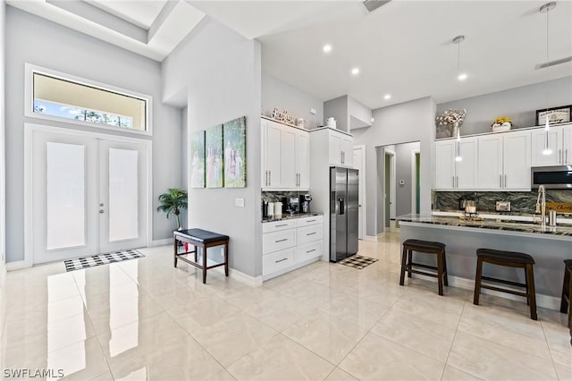 kitchen with appliances with stainless steel finishes, backsplash, a towering ceiling, a breakfast bar, and white cabinets