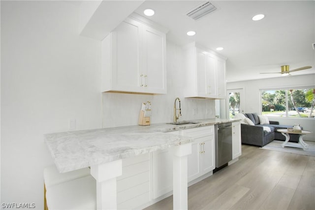 kitchen with dishwasher, kitchen peninsula, sink, white cabinets, and light stone counters