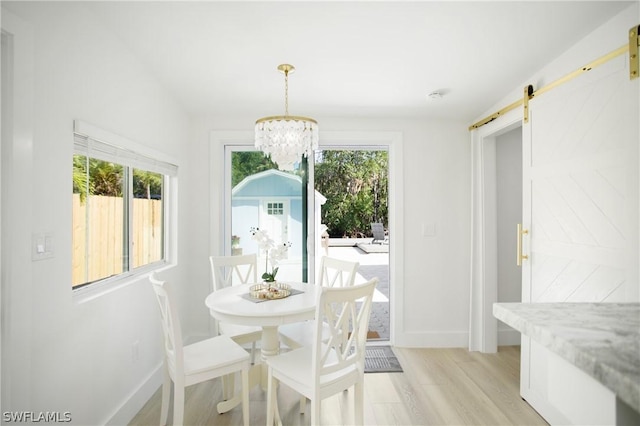 dining room featuring a wealth of natural light, a barn door, light hardwood / wood-style flooring, and a chandelier