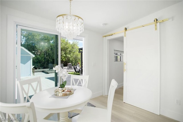 dining space featuring light wood-type flooring, an inviting chandelier, a wealth of natural light, and a barn door