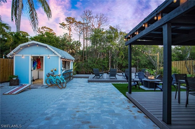 patio terrace at dusk featuring a wooden deck, a storage shed, and a fire pit