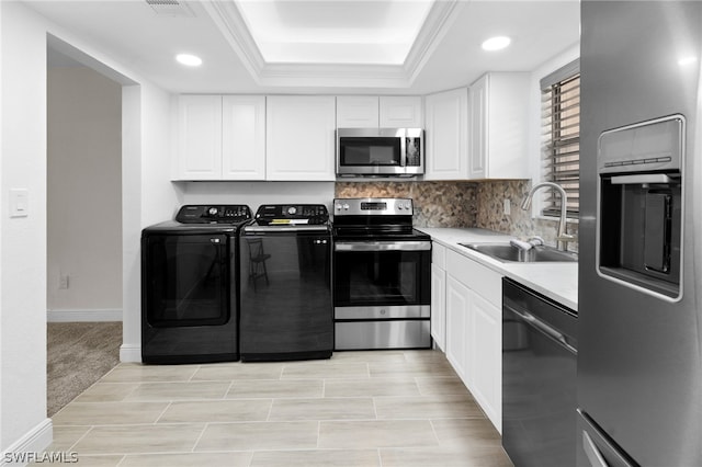 kitchen featuring white cabinets, a tray ceiling, appliances with stainless steel finishes, and washing machine and clothes dryer