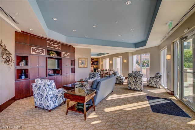 living room featuring light carpet, a tray ceiling, and plenty of natural light