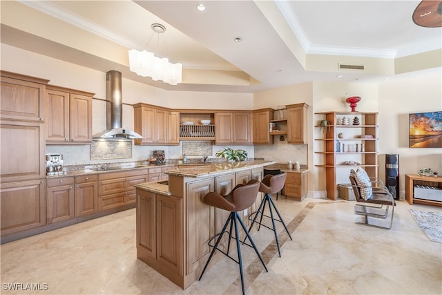 kitchen with a breakfast bar area, a center island, light stone counters, a raised ceiling, and wall chimney exhaust hood