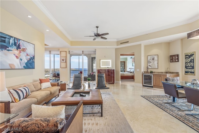 living room with beverage cooler, ceiling fan, a raised ceiling, crown molding, and bar area