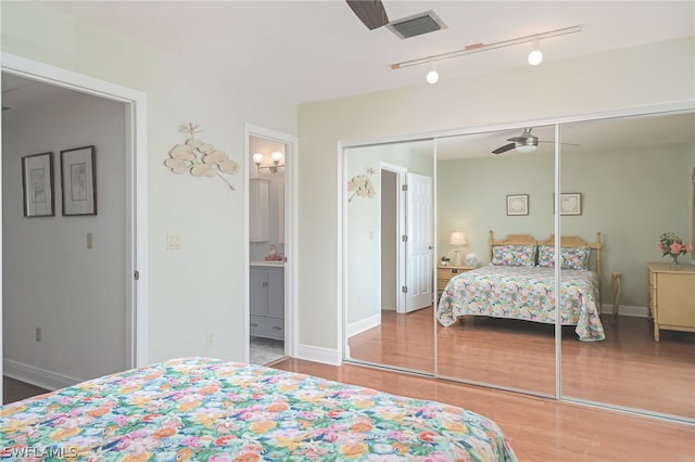 bedroom with a closet, visible vents, ensuite bath, wood finished floors, and baseboards