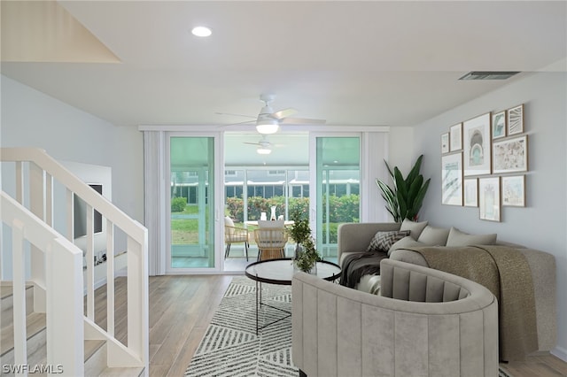 living room featuring visible vents, light wood-style flooring, ceiling fan, expansive windows, and stairs