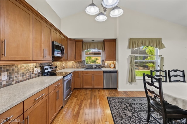 kitchen featuring appliances with stainless steel finishes, hanging light fixtures, decorative backsplash, light wood-type flooring, and a notable chandelier