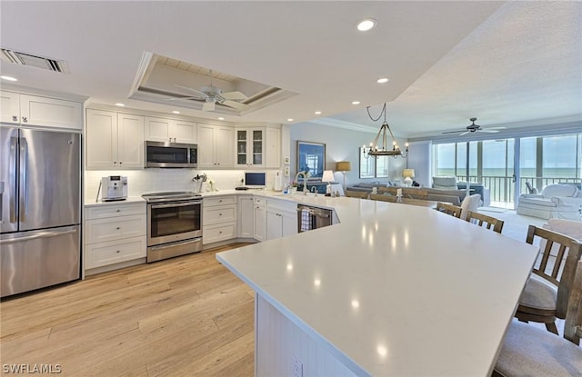 kitchen featuring a breakfast bar, open floor plan, light countertops, appliances with stainless steel finishes, and glass insert cabinets