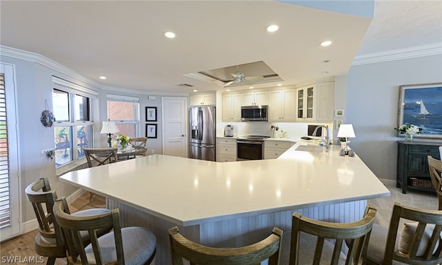 kitchen with a breakfast bar, kitchen peninsula, ceiling fan, appliances with stainless steel finishes, and ornamental molding