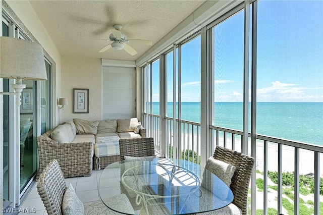 sunroom featuring ceiling fan, a water view, and a view of the beach