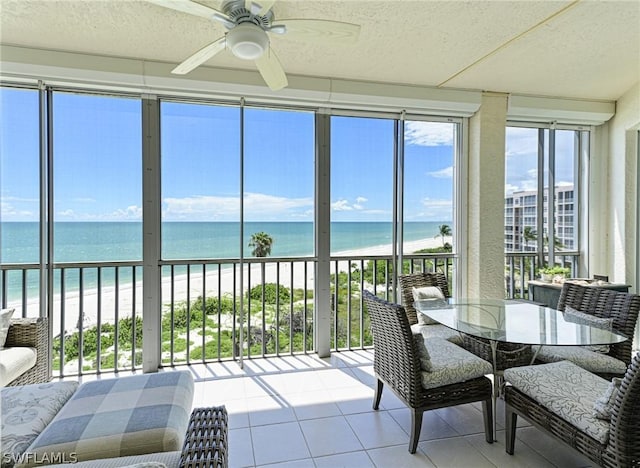 sunroom / solarium featuring a healthy amount of sunlight, a water view, ceiling fan, and a beach view