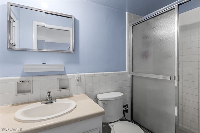 bathroom with vanity, a shower with shower door, tile walls, and toilet