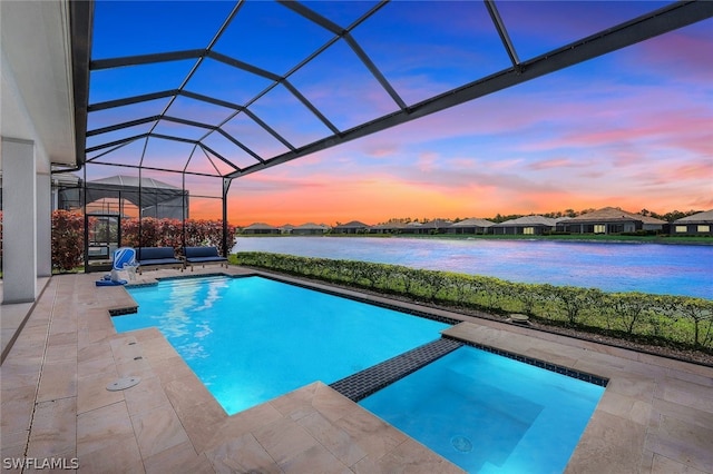 pool at dusk with a lanai, a patio area, a water view, and an in ground hot tub