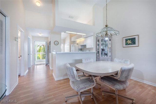 dining area featuring light wood-style floors, visible vents, a towering ceiling, and baseboards