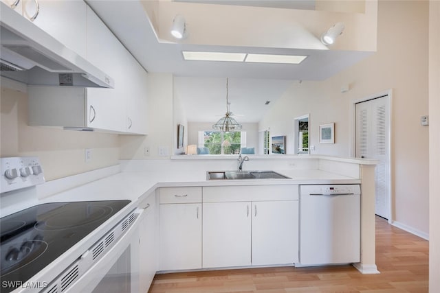 kitchen with white appliances, white cabinets, a peninsula, under cabinet range hood, and a sink