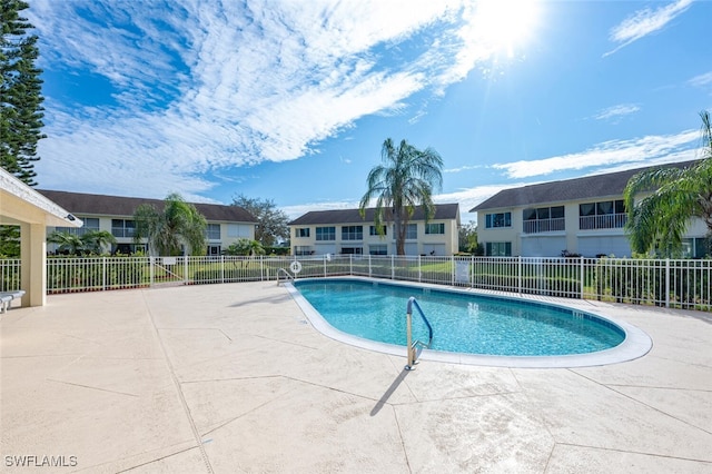 community pool with a patio, fence, and a residential view