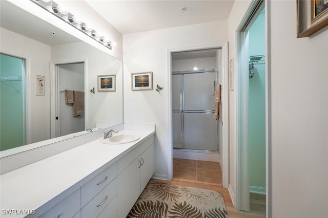 full bath with vanity, a shower stall, a walk in closet, and baseboards