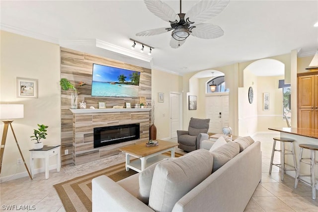 living area with light tile patterned floors, a ceiling fan, a fireplace, arched walkways, and crown molding