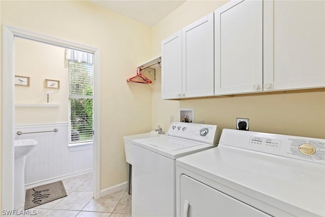 clothes washing area featuring washing machine and dryer, light tile patterned floors, cabinet space, and a wainscoted wall