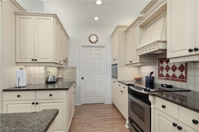 kitchen with custom exhaust hood, dark stone counters, light wood-type flooring, tasteful backsplash, and stainless steel appliances