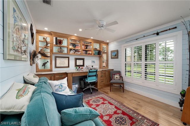 home office with ceiling fan, built in desk, wood walls, and light wood-type flooring