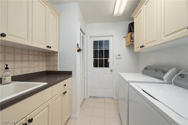 clothes washing area with washing machine and dryer, sink, light tile patterned floors, and cabinets