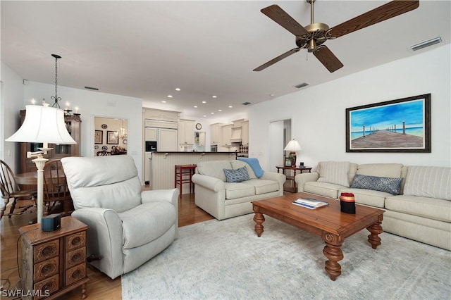 living room featuring ceiling fan with notable chandelier and light hardwood / wood-style floors