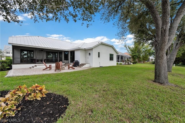 back of property with a sunroom, an outdoor fire pit, a patio area, and a lawn