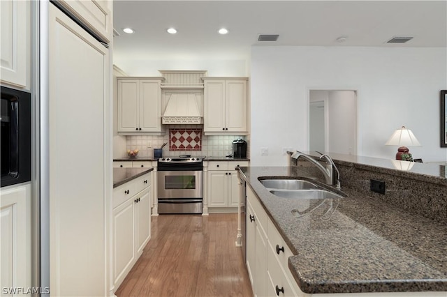 kitchen featuring custom exhaust hood, a kitchen island with sink, dark stone counters, sink, and appliances with stainless steel finishes