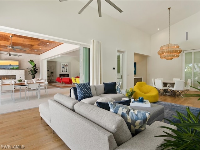 living room with high vaulted ceiling, light hardwood / wood-style flooring, and ceiling fan with notable chandelier