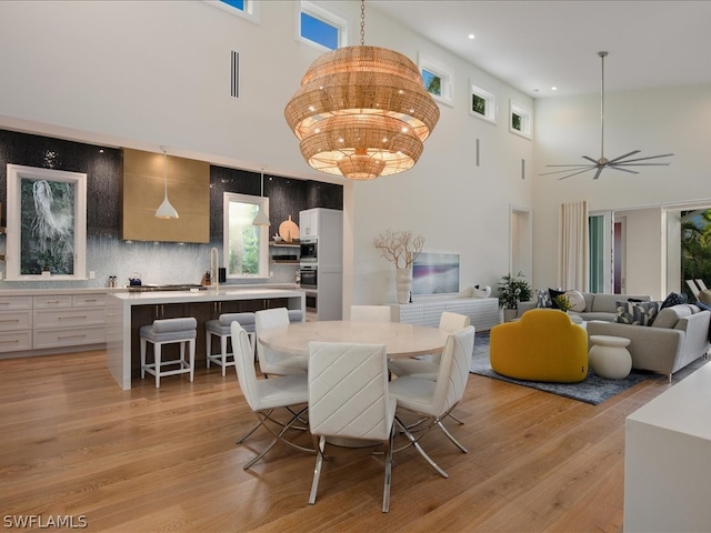 dining area featuring light hardwood / wood-style flooring, a high ceiling, and ceiling fan with notable chandelier