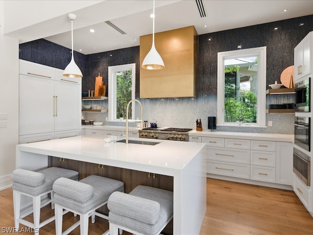 kitchen featuring light hardwood / wood-style floors, white cabinetry, a kitchen island with sink, and hanging light fixtures